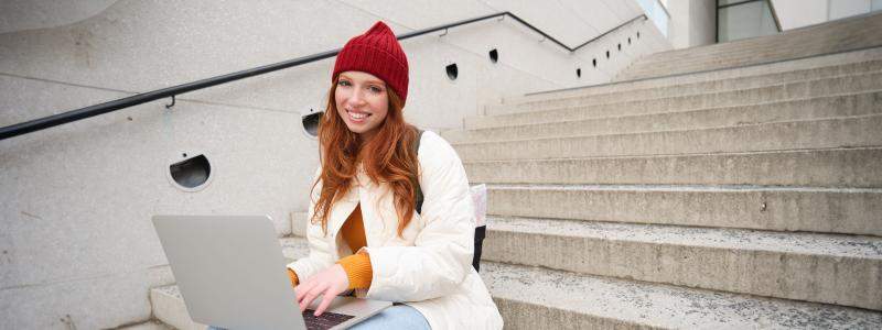 smiling-redhead-girl-young-woman-typing-laptop-keyboard-sitting-outdoors-stairs-with-computer-rsz